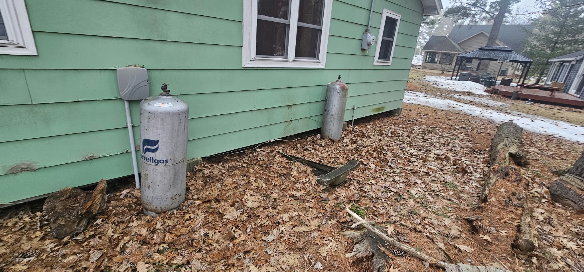 Before — original exterior, worn siding and propane tanks, Bone Lake cabin