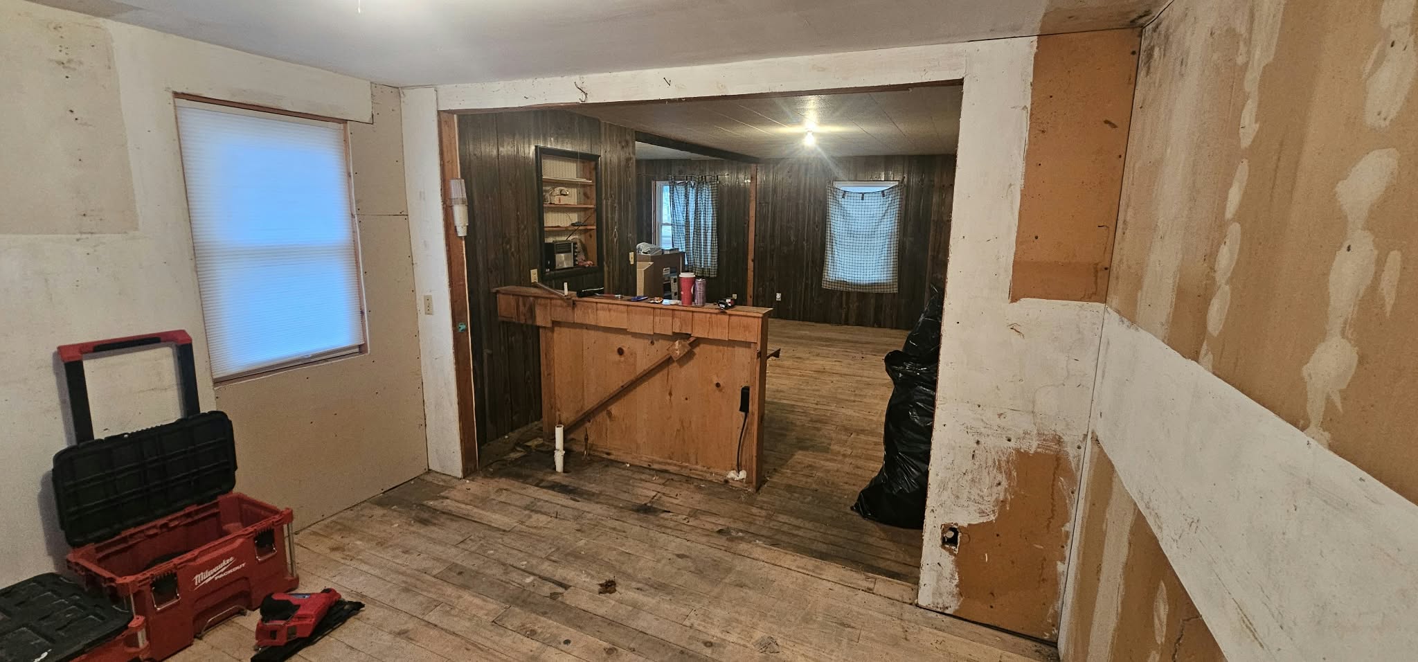 Before — mid-demo, dark wood paneling and original plank floors